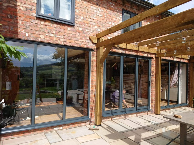 Modern house exterior with large glass windows and a wooden pergola.