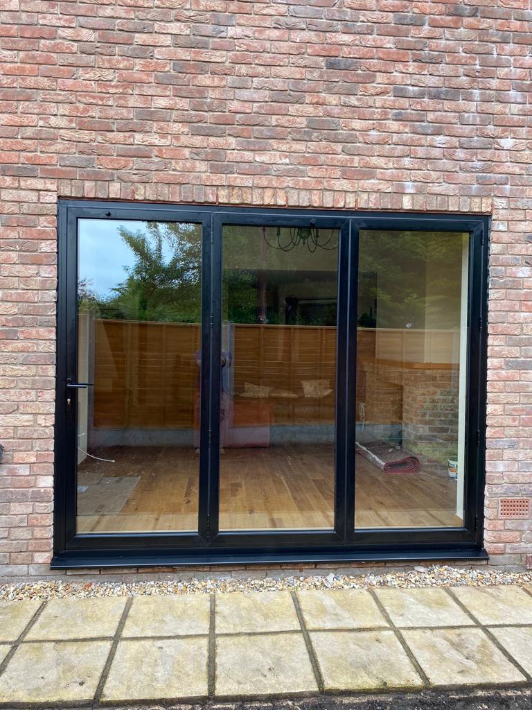 Black-framed glass door on a brick wall with a view of a garden.