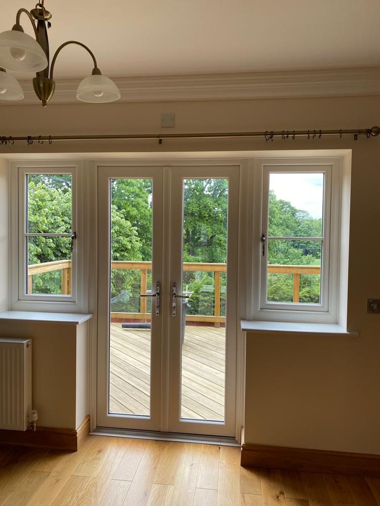 Living room with white French doors leading to a deck, surrounded by windows.