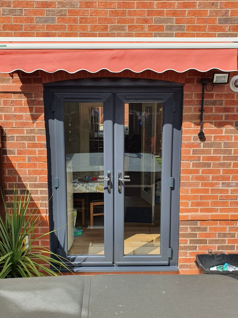 Gray French doors with a red awning on a brick wall