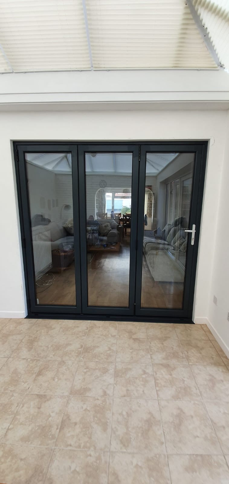 Black-framed sliding glass door leading to a sunlit room with furniture.