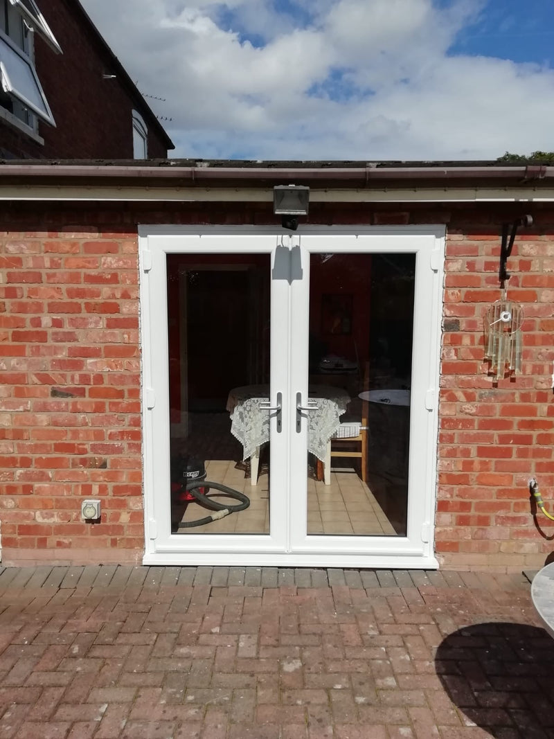 White double doors leading to a patio area on a brick building with a blue sky.