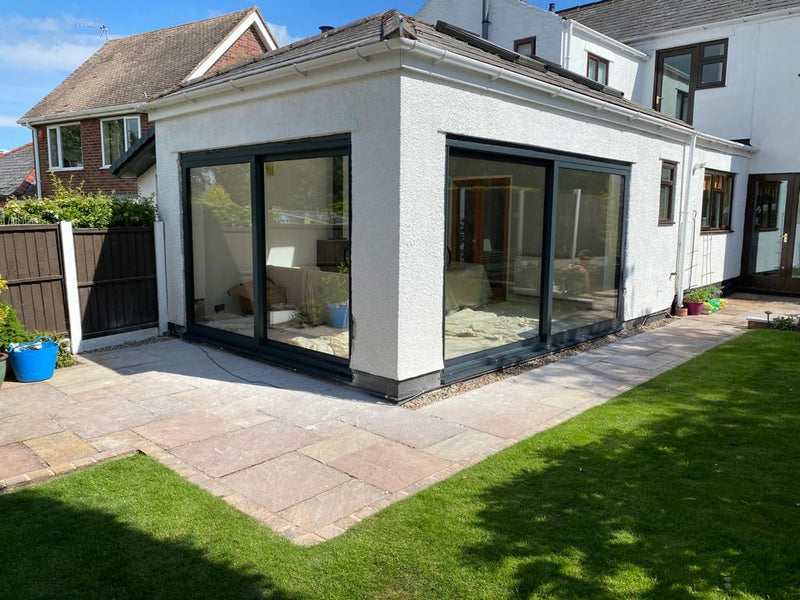 Modern extension of a house with large glass windows, surrounded by a garden.